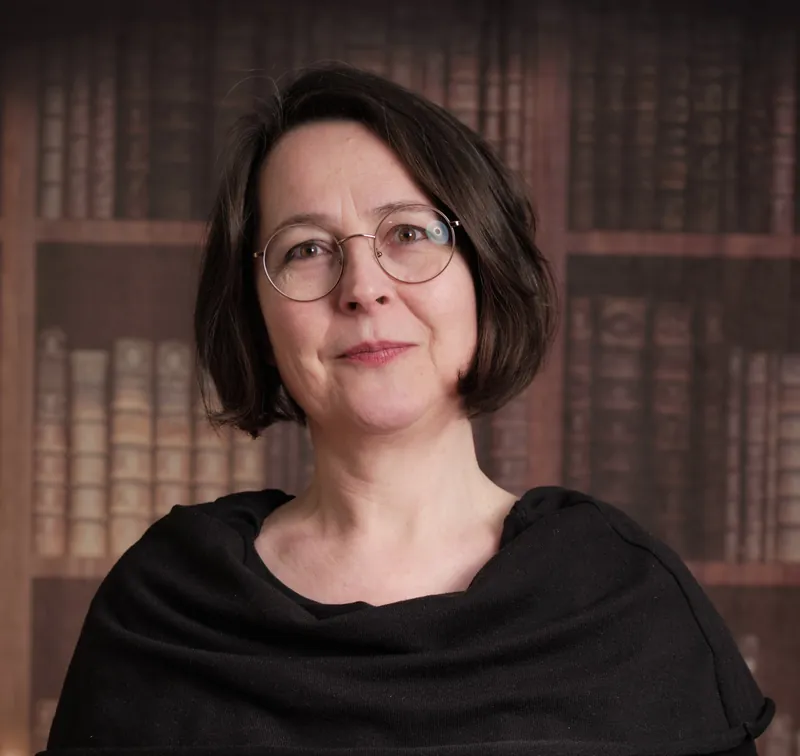 Porträt von Xenia Busam vor einer Bücherwand, Erzählerin und Dozentin